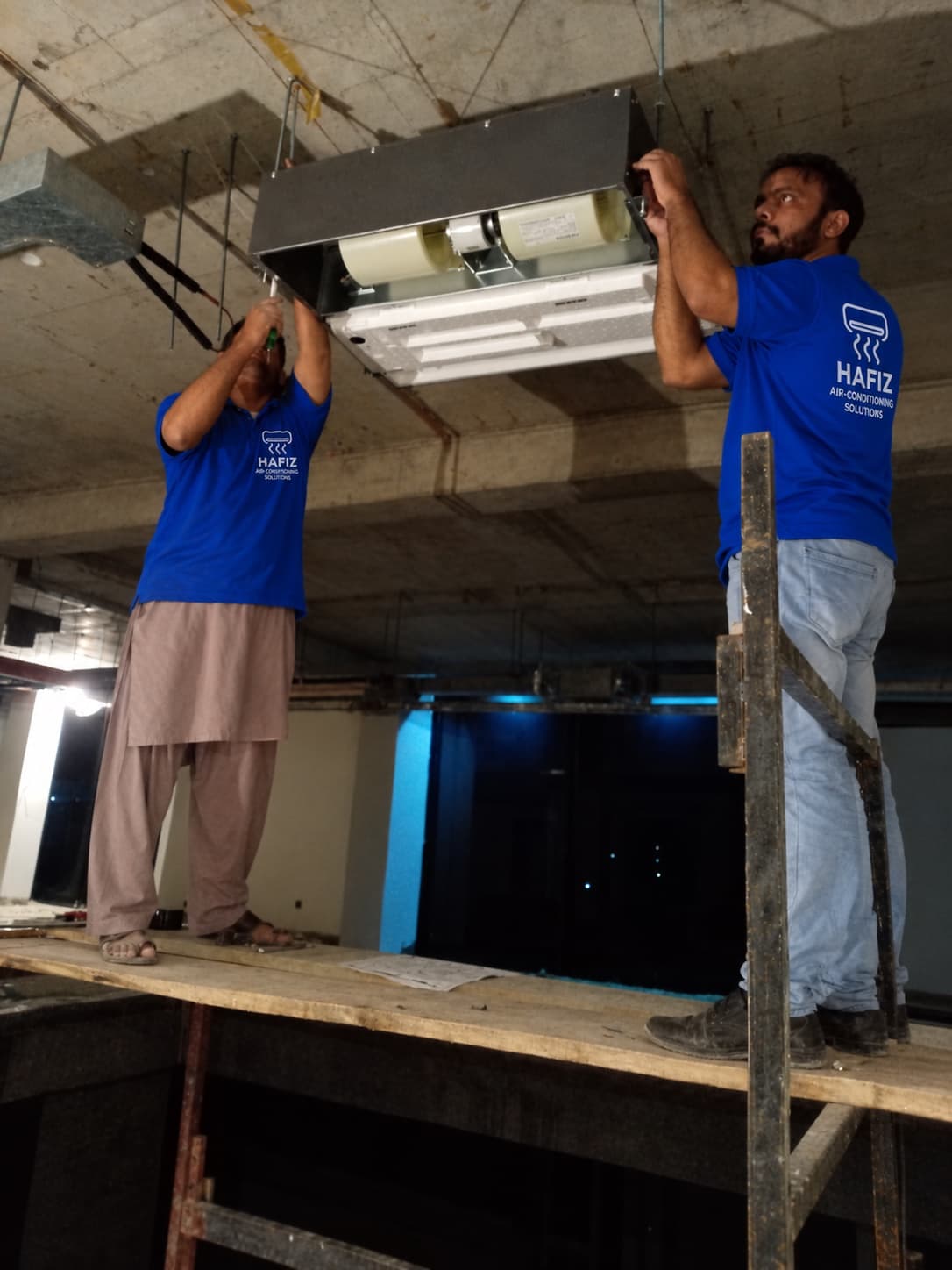 Technicians mounting Hitachi concealed indoor fan coil unit on site